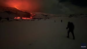 Hikes walk in the snow past an erupting Mt. Etna