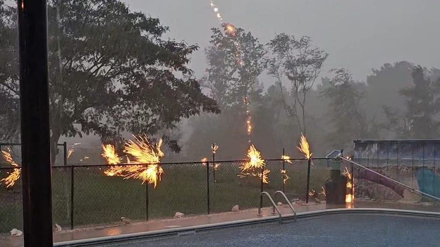Lightning strikes tree, sending sparks flying along nearby fence