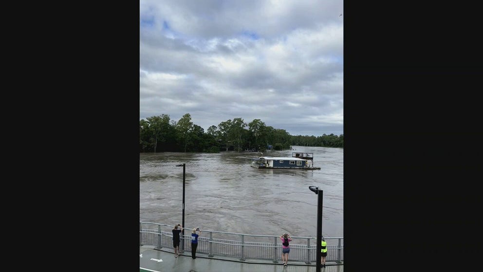 A houseboat broke free during flooding on the Brisbane River in Queensland and was swept downstream in the swift current narrowly missing bridge pilings.
