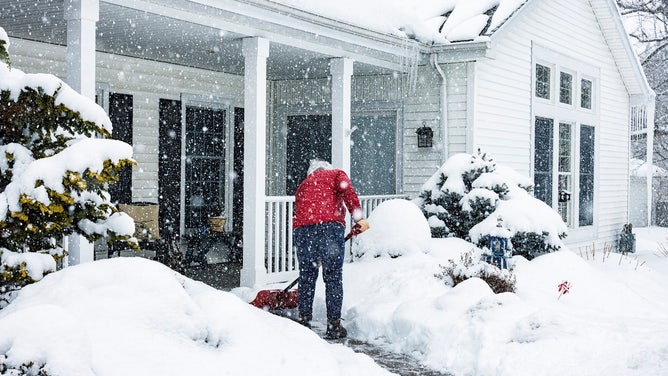 person shoveling snow outside of home using a shovel