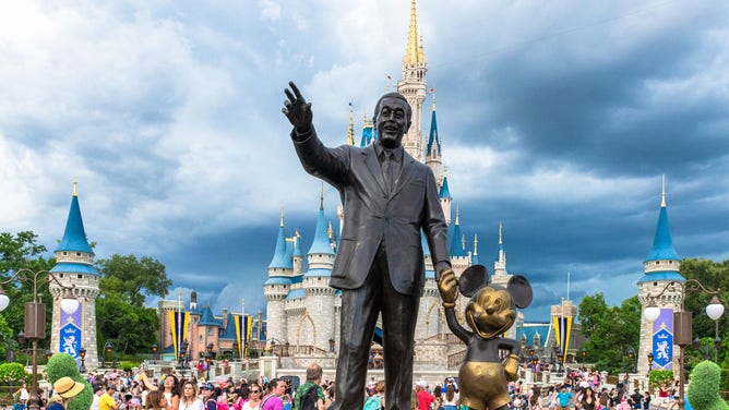 Walt Disney and Mickey Mouse statue inside of the Magic Kingdom theme park . The Cinderella castle can be seen in the background.