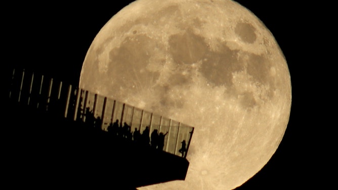 People standing on the Edge NYC outdoor observation deck are silhouetted by the full Hunter's Moon rising in New York City on October 20, 2021 as seen from Hoboken, New Jersey. Earlier in the day Related Companies, the owner of Hudson Yards announced KKR &amp; Co. bought a majority stake in EdgeNYC. (Photo by Gary Hershorn/Getty Images)