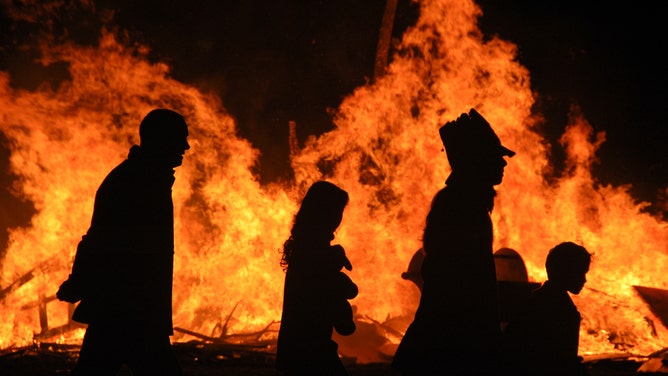 A family is silhouetted by a bonfire on Halloween night.