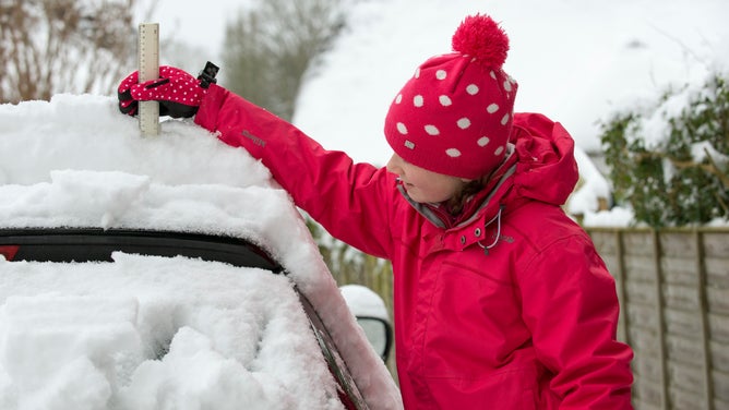Young girl checks the snow depth on a car using a ruler