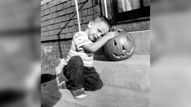 A boy sits next to his Halloween jack-o'-lantern pumpkin