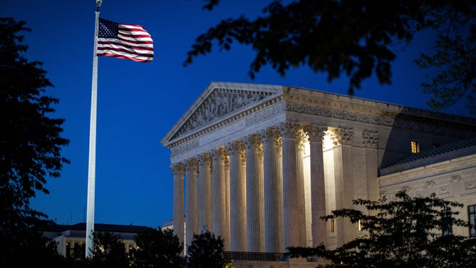 An American flag flies outside the U.S. Supreme Court as it stands illuminated at night.