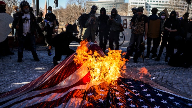 A U.S. flag is placed on the ground and set on fire.