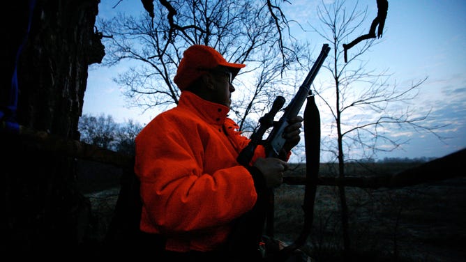 A hunter holds his rifle while seated in a tree stand before sunrise on the opening morning of the Wisconsin whitetail deer season.