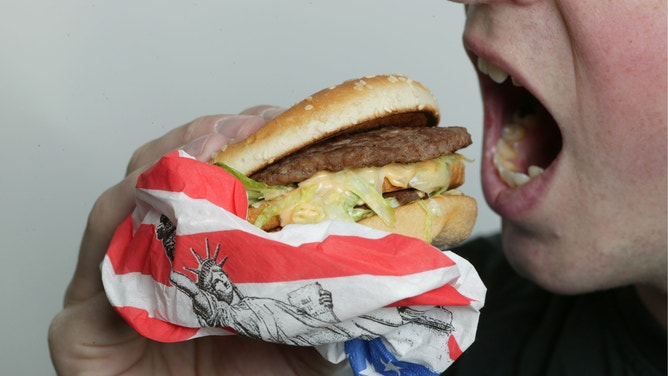 Man eats a hamburger partially encased in a wrapper with a U.S. flag pattern.