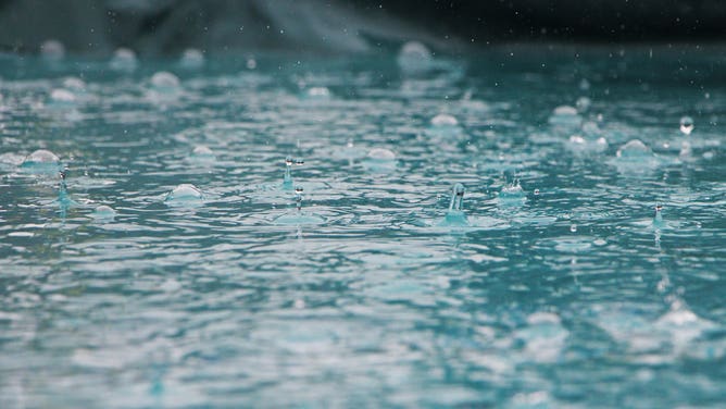 Rain falls onto a pool of water.