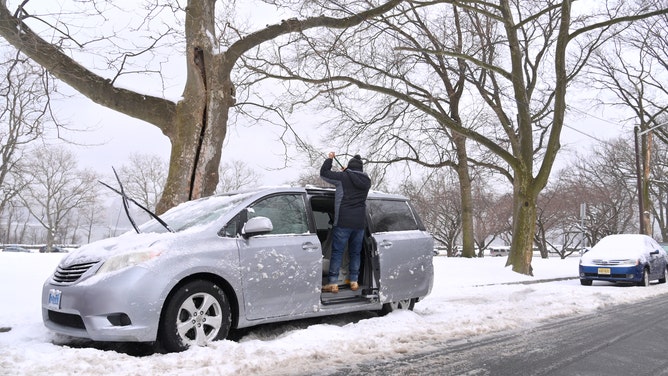 A man brushes snow off the roof of his car at James J. Braddock Park on Feb. 18, 2021, in North Bergen, New Jersey.