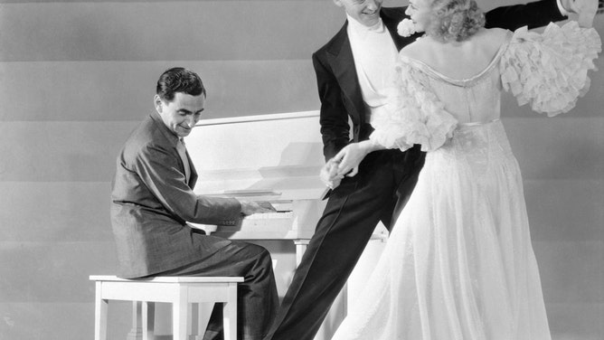 Irving Berlin plays the piano for screen dancers Fred Astaire and Ginger Rogers. Berlin wrote the music for several Hollywood musicals in which the famous dancing duo appeared.