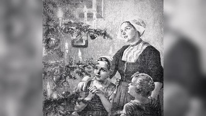 Christmas time, mother and two children in front of Christmas tree with burning candles.