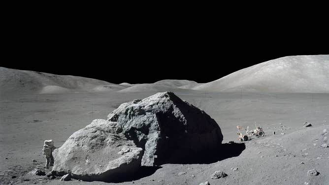 On Dec. 13, 1972, scientist-astronaut Harrison H. Schmitt is photographed standing next to a huge, split lunar boulder during the third Apollo 17 extravehicular activity (EVA) at the Taurus-Littrow landing site. The Lunar Roving Vehicle (LRV), which transported Schmitt and Eugene A. Cernan to this extravehicular station from their Lunar Module (LM), is seen in the background. The mosaic is made from two frames from Apollo 17 Hasselblad magazine 140. The two frames were photographed by Cernan.