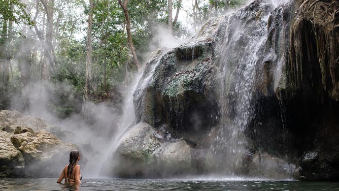 A woman swims near a cascade of steaming hot springs
