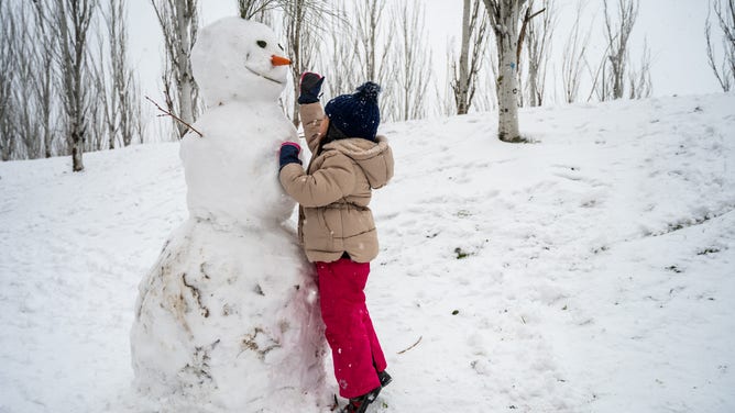 A girl builds a snowman as snow falls in a park in Spain.