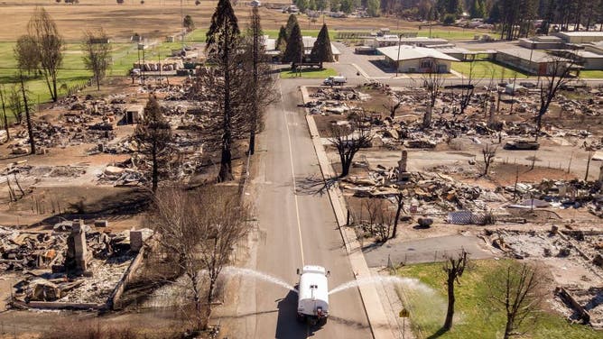 An aerial picture taken on September 24, 2021 a water truck sprays down the burned remains of downtown Greenville, California.