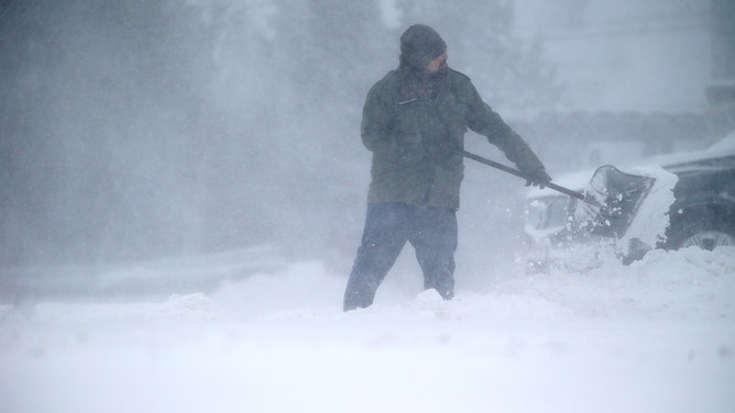 FILE - High winds and blowing snow did not stop some from shoveling out in Hull, Massasschuttes, on Jan. 29, 2022, in near whiteout conditions. A large storm bears down on New England, bringing one to two feet of snow, along with high winds, cold temperatures in the largest NorEaster in recent years.