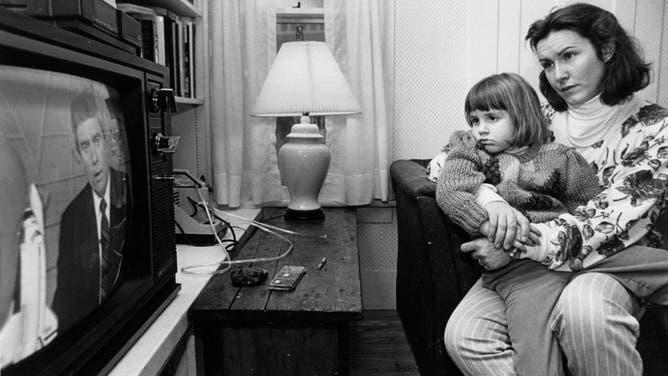Mandana Marsh holds her daughter, Molly, 4, as they watch television coverage hours after the explosion of the space shuttle Challenger inside their home in Concord, N.H., Jan. 28, 1986. When her mother explained what happened, Molly asked, "Can't Christa swim?" (Photo by Suzanne Kreiter/The Boston Globe via Getty Images)
