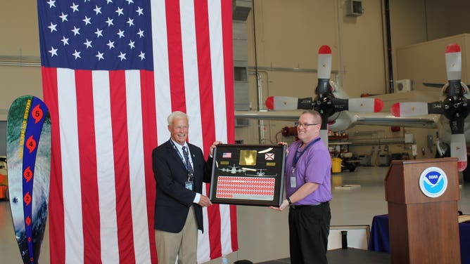 Jack Parrish receives plaque commemorating his 42 years of service with stickers for each of the 103 hurricanes he flew through, from Allen in 1980 to Larry in 2021. (Credit: NOAA)