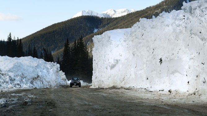 An SUV drives through a pass, flanked by snowbeds created from a recent avalanche.