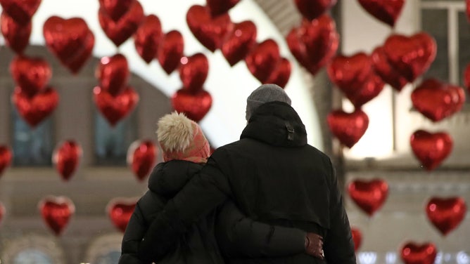 A man and woman walk toward heart-shaped balloons on the eve of Valentine's Day.