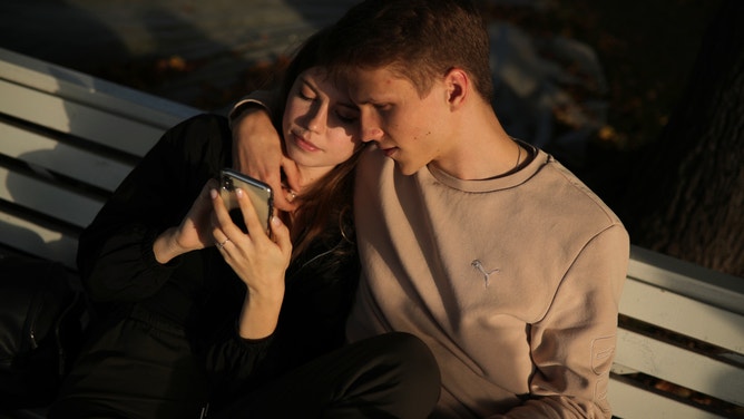 A couple sit on a bench on an autumn day.