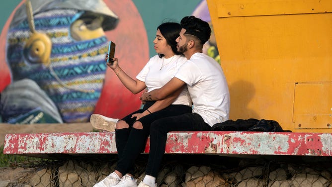 A couple takes a selfie next to a mural.