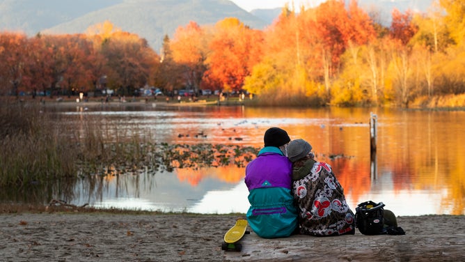 A couple sits by a lake on a chilly autumn day.