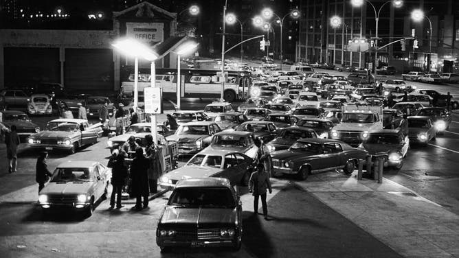 In 1973 Brooklyn, NY, a large crowd of cars lined up for gas at filling station on Saturday night during gas shortage crisis.
