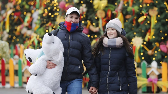 A couple holds hands with Christmas decorations in the background.