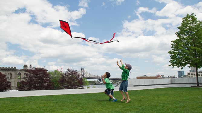 Children chase after a red diamond kite.