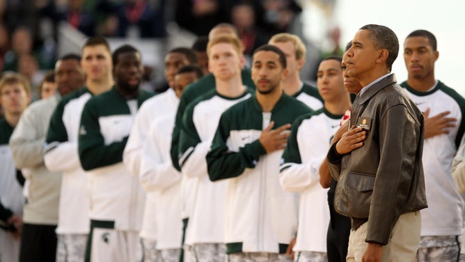 U.S. President Barack Obama and first lady Michelle Obama stand next to the Michigan State Spartans during the United States National Anthem before the start of the NCAA men's college basketball Carrier Classic between the Spartans and the North Carolina Tar Heels aboard the flight deck of the USS Carl Vinson on November 11, 2011, in San Diego, California.