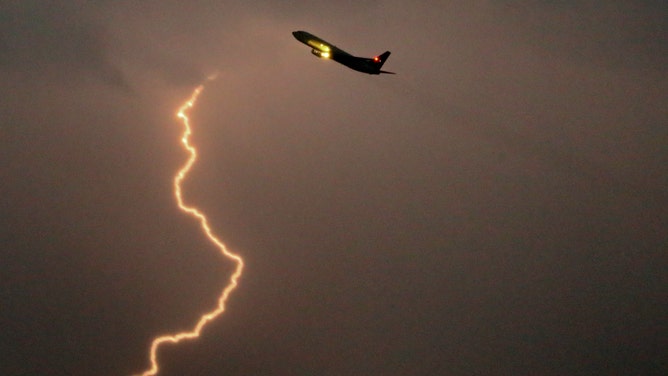 Lightning strikes well in the distance of a departing jet at Boston's Logan Airport.