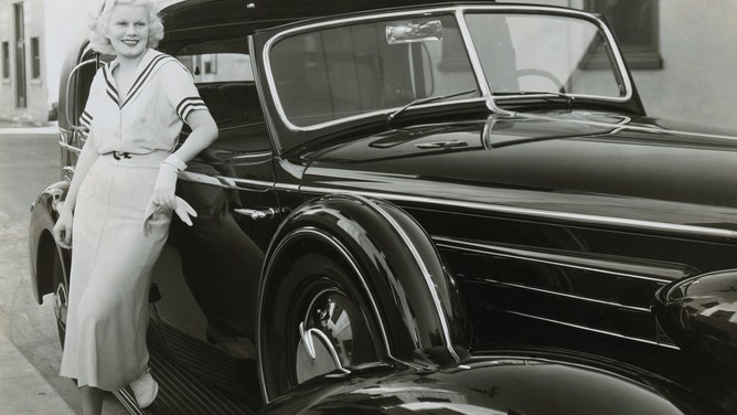 Actress Jean Harlow poses next to a car with windshield wipers in the early 1930s.
