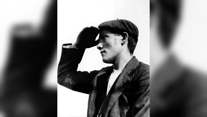 An Irish immigrant wears a beret and shields his eyes in order to catch a glimpse of New York City across the harbor, Ellis island, early 20th Century.