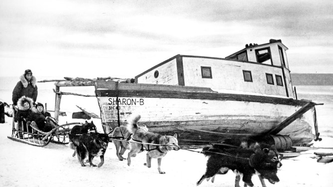 Alaska Natives on a sled pulled by their dogs.