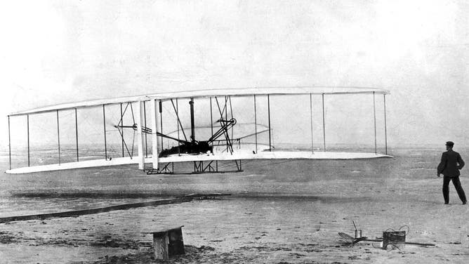Orville Wright, stretched out face-down on the lower wing panel of the Wright brothers' Kitty Hawk, makes man's first flight in a powered plane.