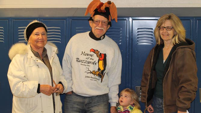 On Buzzard Day, a little girl looks up at a man wearing a buzzard hat and a sweater saying 'Home of the Buzzards Hinckley, Ohio'.