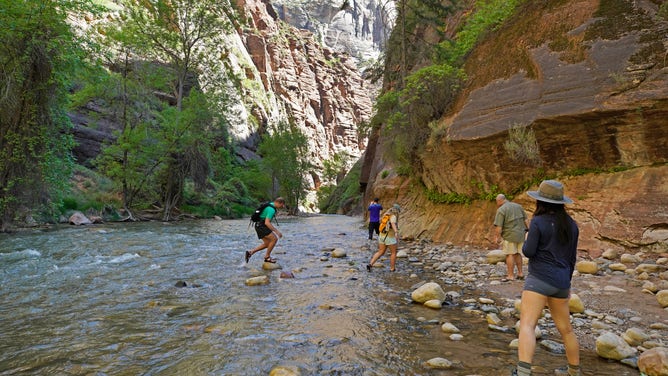 Hikers take pictures at the entrance of the famous Narrows hike in Zion National Park.