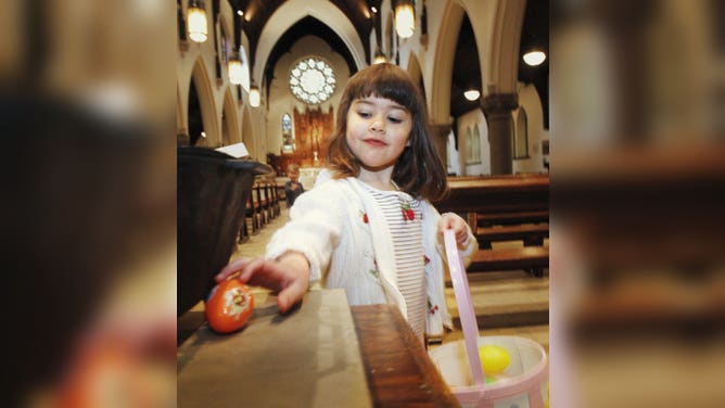 A little girl finds an orange egg during an Easter egg hunt at church.
