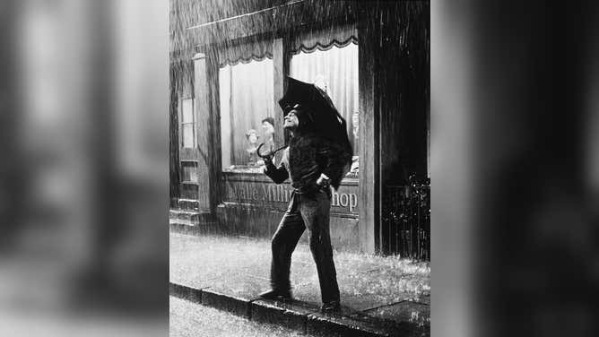 A light casts a glow on Gene Kelly's face as he stands in the "rain" in this production still.