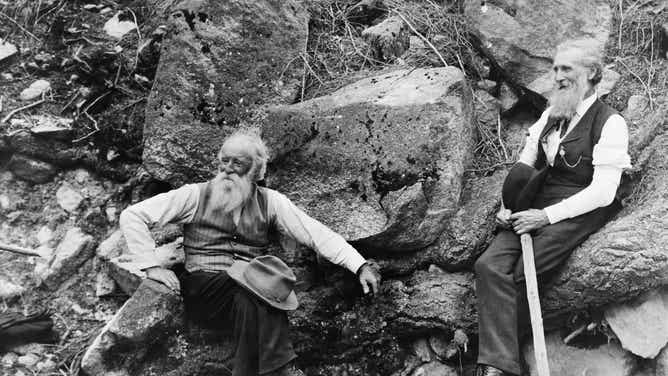 Naturalists John Burroughs and John Muir seated on a group of large rocks. The two helped pioneer the early conservation movement in the U.S. in the late 19th and early 20th centuries.