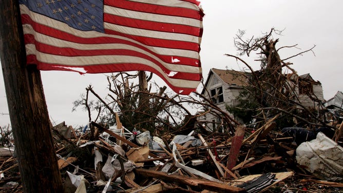 A flag was attached to a telephone pole, May 6, 2007, in front of a home devastated by the Greensburg, Kansas, tornado. Less than three months later, the debris and the dwelling are gone, as the cleanup process continues.