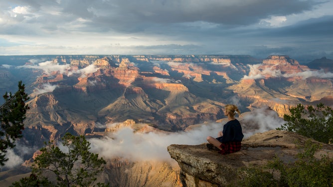 A young woman sits peacefully at the Grand Canyon.