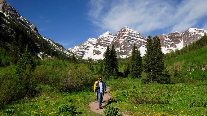 A couple visiting from India walk along a Colorado nature trail with the Maroon Bells as a dramatic backdrop. The Maroon Bells are two peaks in the Elk Mountains - Maroon Peak and North Maroon Peak. They are located in the Maroon Bells-Snowmass Wilderness of White River National Forest.