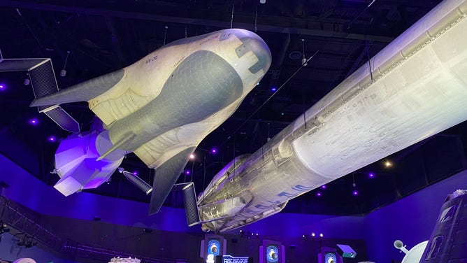 A Sierra Space Dreamchaser and SpaceX Falcon 9 suspended from the ceiling at Kennedy Space Center Visitor Complex.