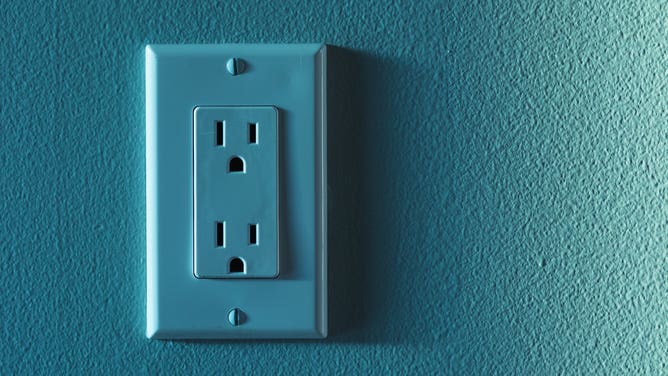 A teal electric outlet on a teal wall.