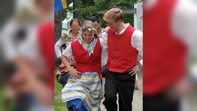 Young men and women dance in traditional Swedish dress.