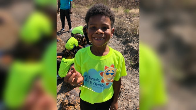 A young boy smiles as he holds an Astrodon tooth.